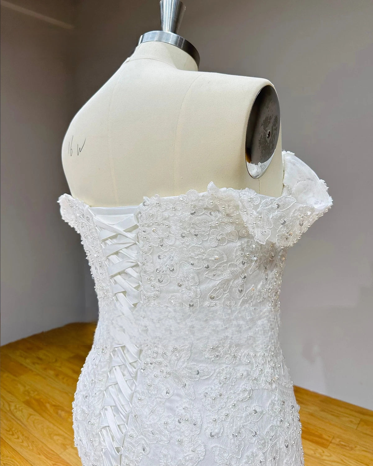 Side profile view of a mermaid bridal gown bodice showcasing the adjustable ribbon corset closure and textured floral lace detailing with pearl embellishments.