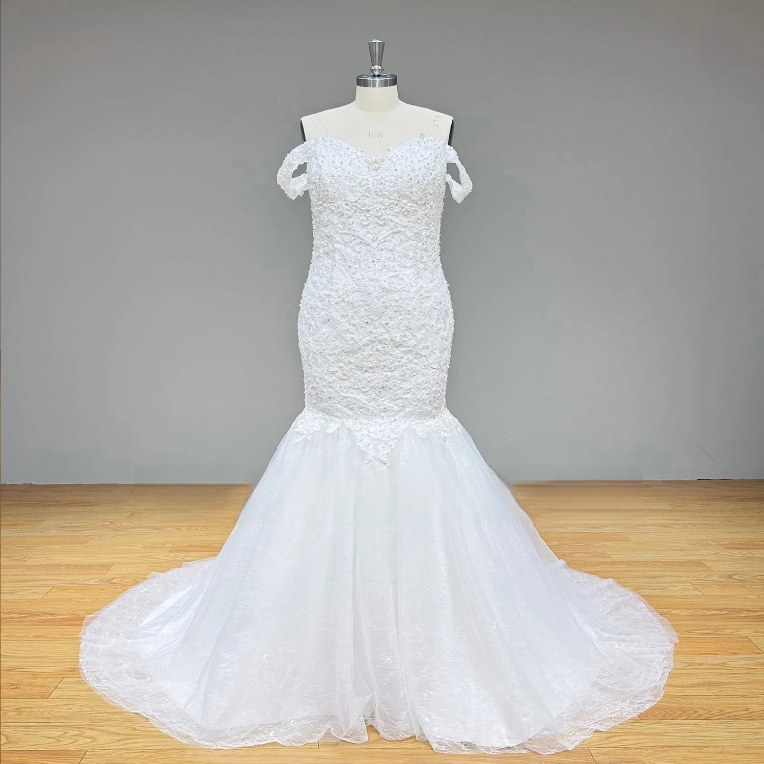 Full front studio view of a white lace and tulle mermaid wedding dress featuring a beaded drop-waist silhouette on a dress form.