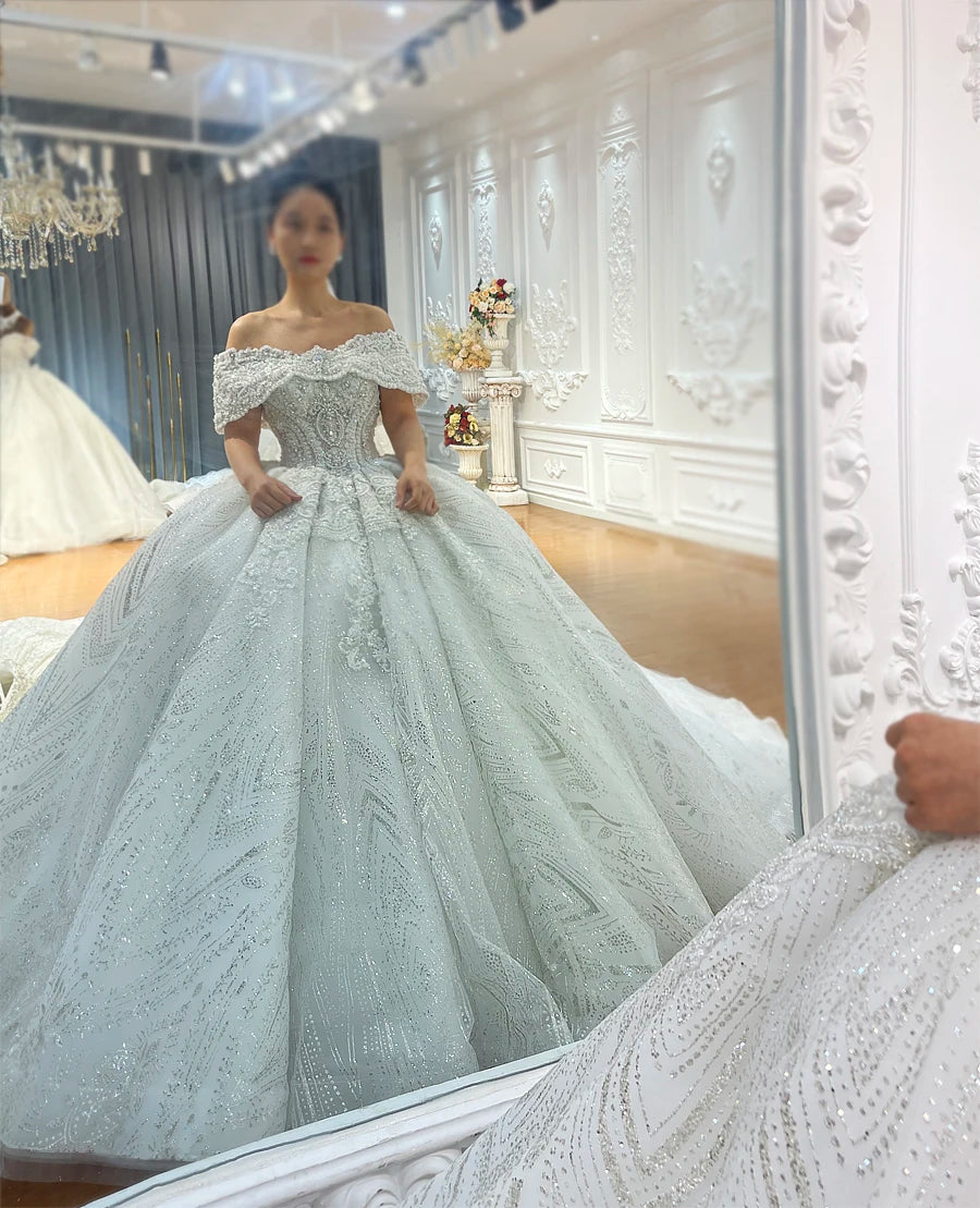 Side profile of a luxury off-the-shoulder ball gown with a full skirt and shimmering silver embroidery in a studio setting.
