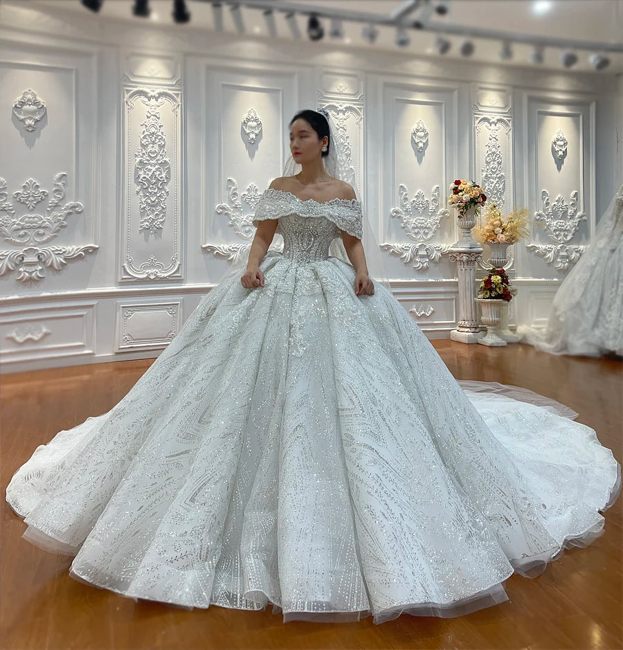 Front view of a romantic off-the-shoulder bridal gown with a voluminous sparkling skirt and detailed sequin patterns.