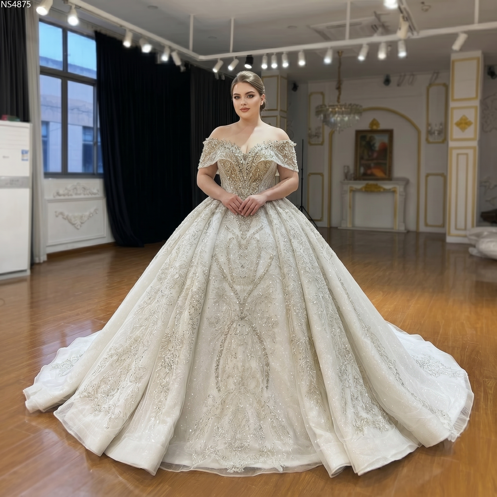 A curvy bride showcasing the elegant off-the-shoulder beaded wedding gown with heavy crystal embellishments and a deep sweetheart neckline.