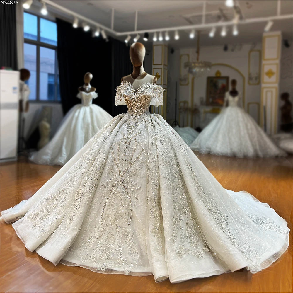 Front view of a luxury off-the-shoulder beaded wedding gown on a mannequin, featuring an elegant ball gown silhouette and intricate sparkling embellishments.