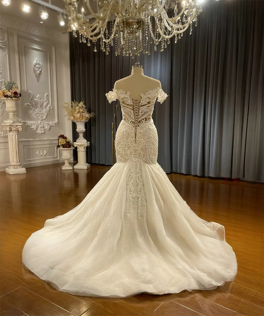 Rear view of the off-the-shoulder mermaid wedding dress on a mannequin, showing the elegant corset back and the expansive, flowing lace train.