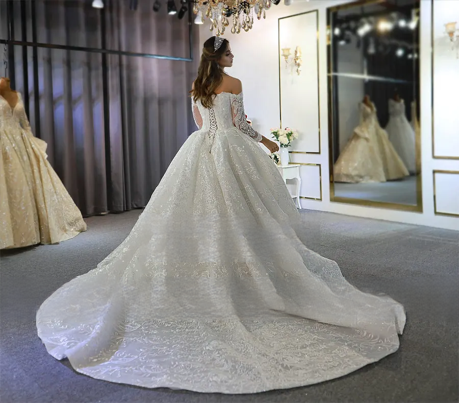 Front view of an off-the-shoulder long sleeve lace wedding dress featuring a sweetheart neckline and shimmering floral embroidery.