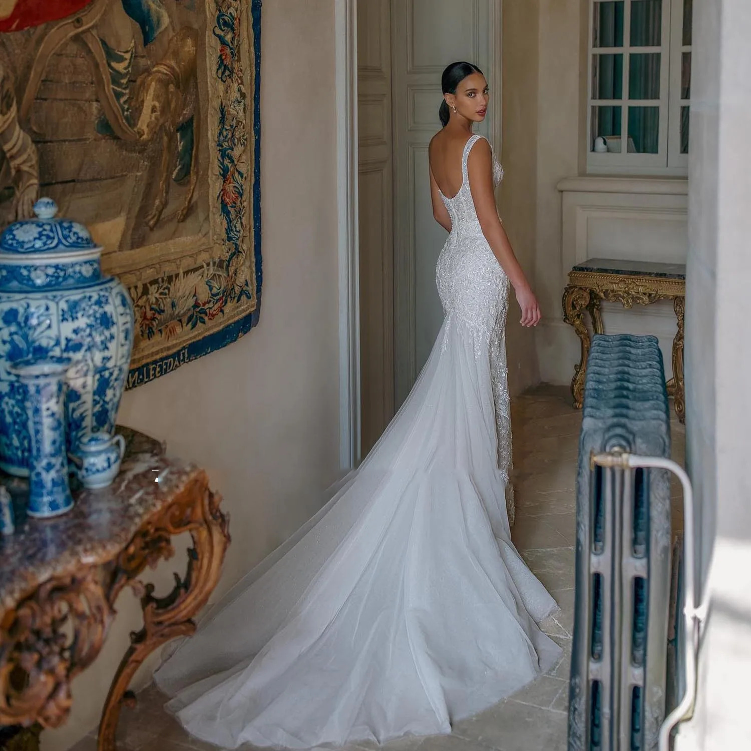 Rear profile of a backless lace mermaid wedding dress showcasing a low scoop back, textured floral appliques, and a pooling tulle trumpet train.
