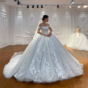Full-length view of an off-the-shoulder off-white wedding dress featuring flowing floral vine lace and a voluminous ball gown silhouette.