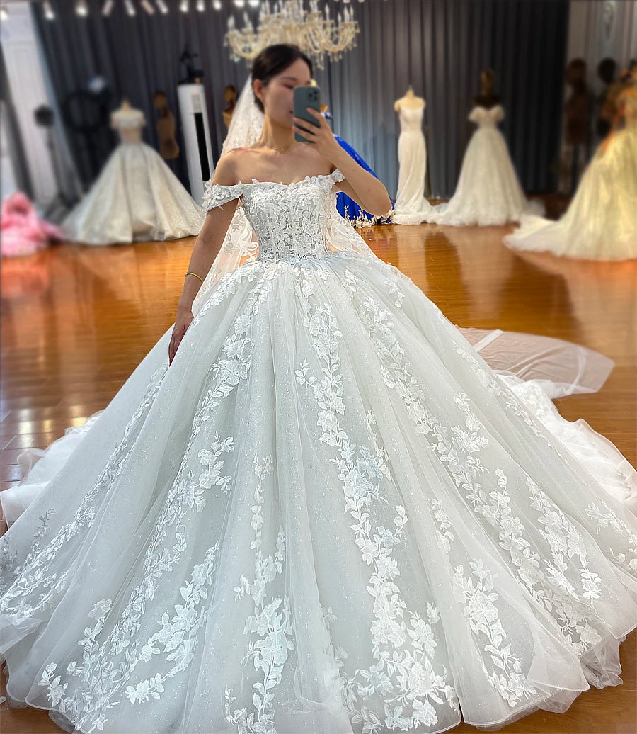 Front view of a strapless off-white bridal gown with intricate floral lace embroidery on a structured bodice and a shimmering full skirt.