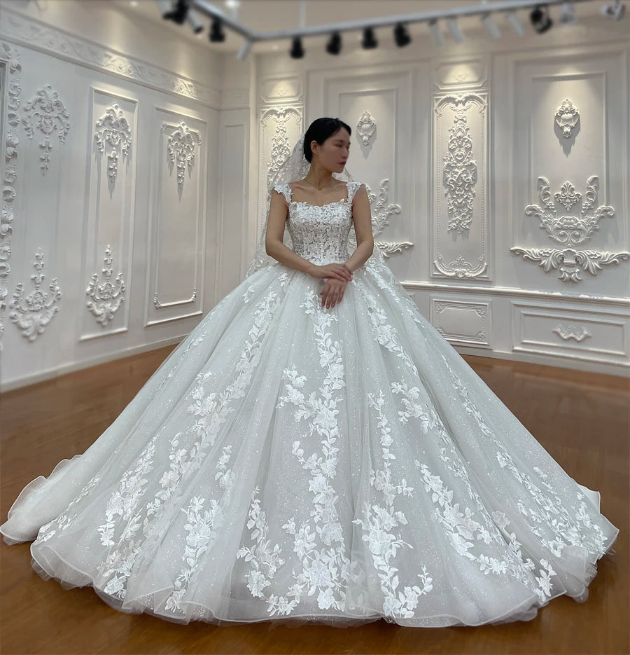 Front-facing view of an elegant off-white wedding dress with thick floral lace straps and a wide, embroidered A-line skirt.