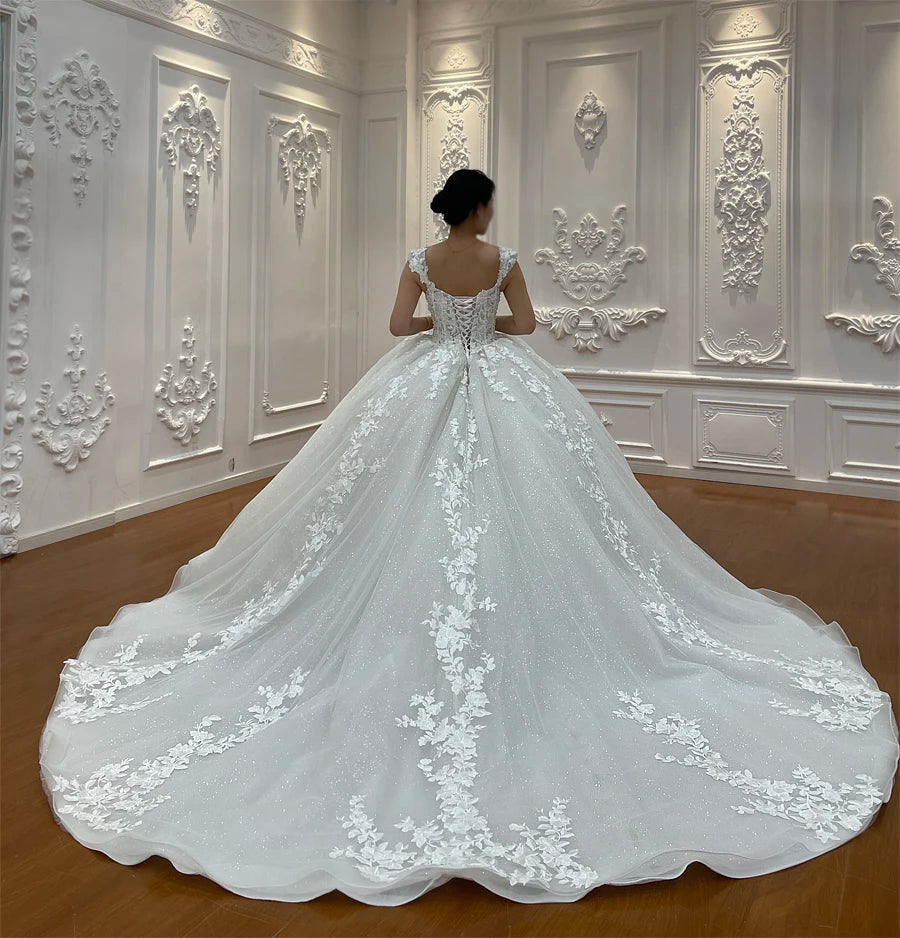 Back view of an off-white bridal gown highlighting a traditional lace-up corset back and trailing floral vine embroidery on the train.