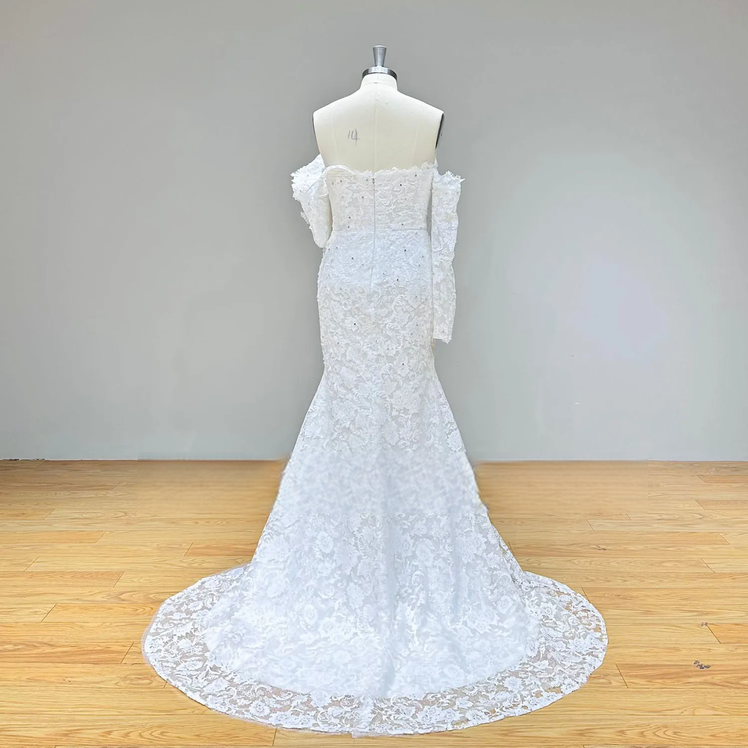 Back profile of an elegant fitted lace mermaid wedding gown on a mannequin, highlighting the fit-and-flare silhouette and detailed floral lace embroidery without the overskirt.