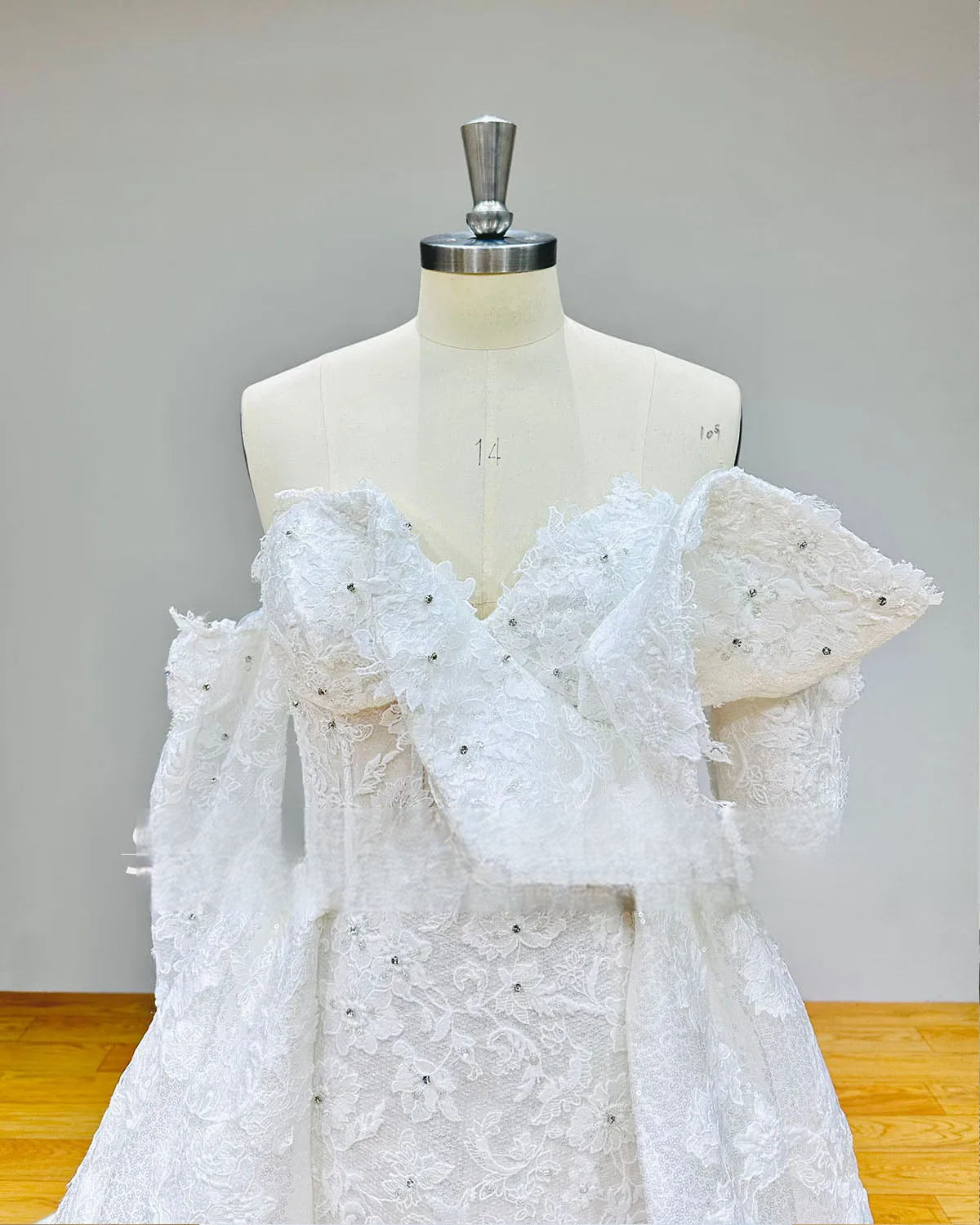 Close-up detail of the off-shoulder bodice on a 2-piece mermaid bridal gown, showcasing unique ruffled lace detailing, subtle crystal beading, and semi-sheer corset-style boning.