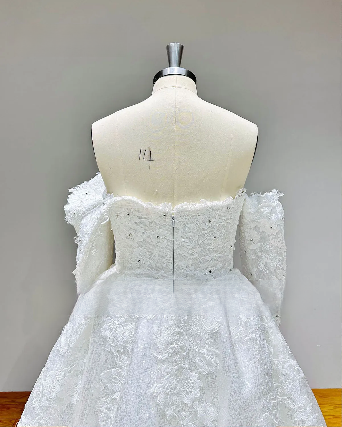 Close-up of the back of a beaded lace bridal gown bodice, illustrating the delicate lace craftsmanship, crystal accents, and clean zipper-back closure.