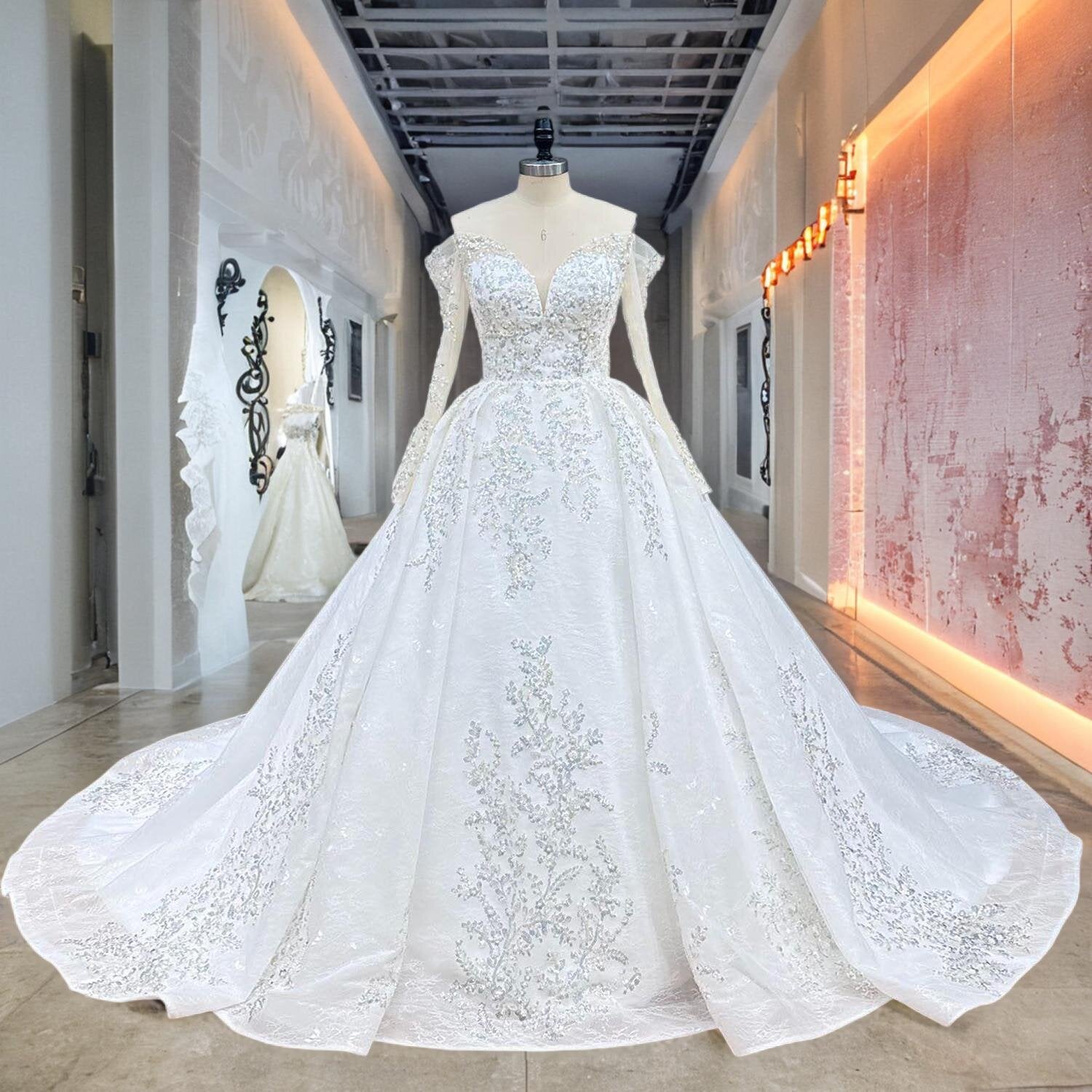 Full front view of an off shoulder ball gown wedding dress on a mannequin in a bright hallway, perfectly displaying the regal silhouette, sheer long sleeves, and a sweeping skirt decorated with beading and pearls.