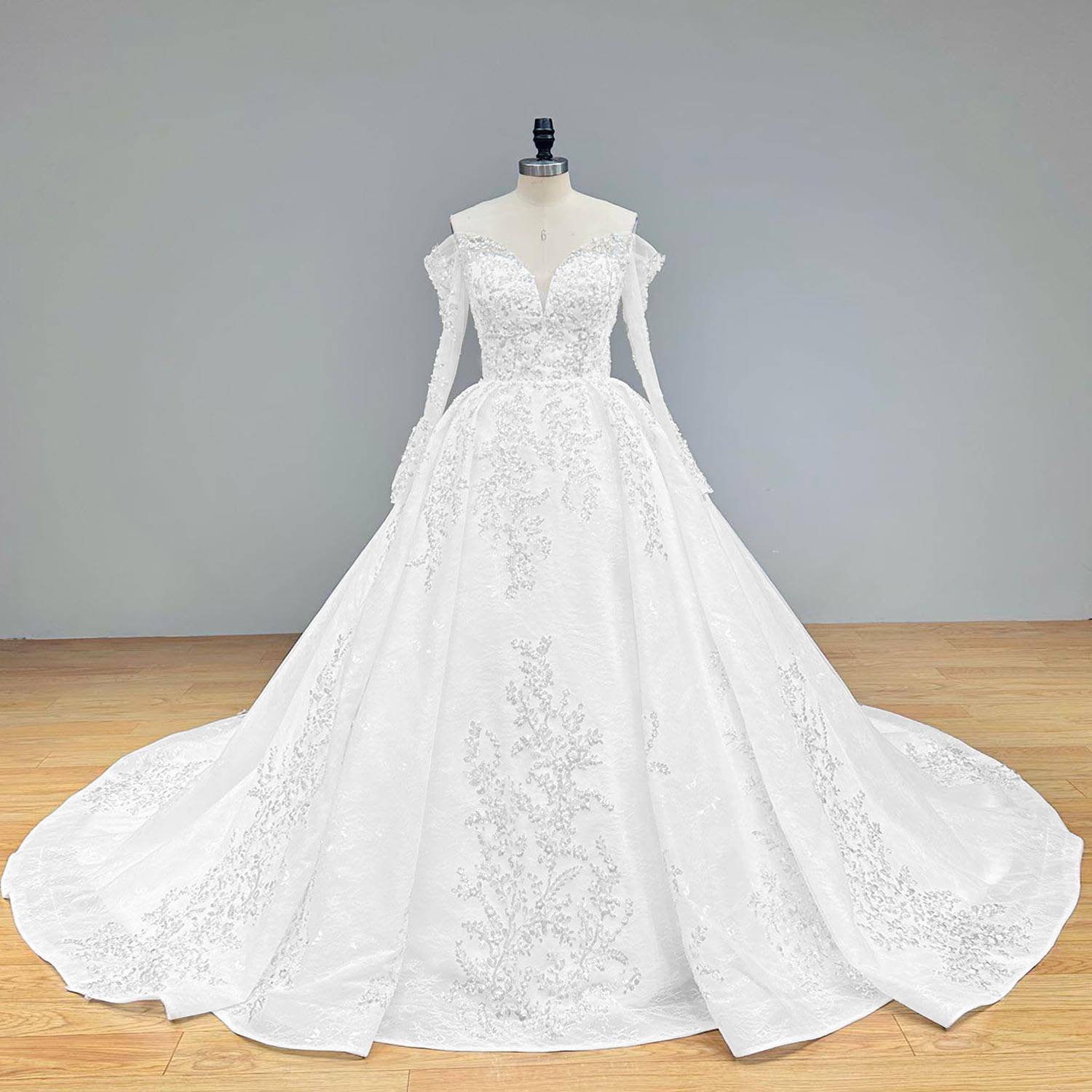 Wide front studio view of an elegant off shoulder ball gown wedding dress on a mannequin, perfectly capturing the heavily embellished bodice with beading and pearls, sheer long sleeves, and a wide flowing train.