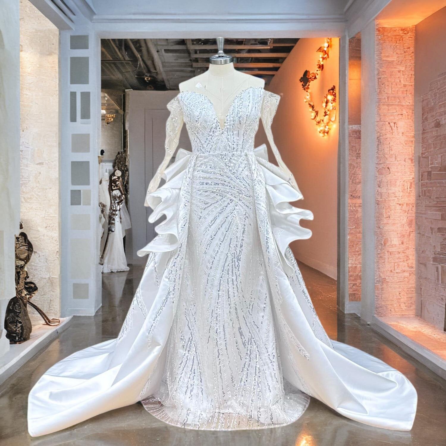 Front studio display of an off-shoulder mermaid bridal dress on a mannequin, highlighting the fitted bodice, long lace sleeves, and a stunning detachable train.