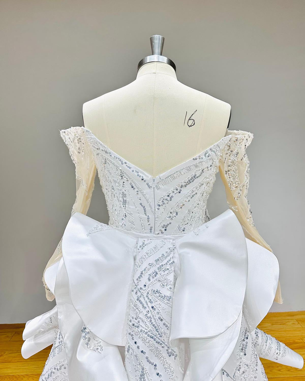 Back view of a mermaid wedding dress on a mannequin, showcasing the illusion lace back, intricate beadwork, and the full length of the detachable cathedral train.
