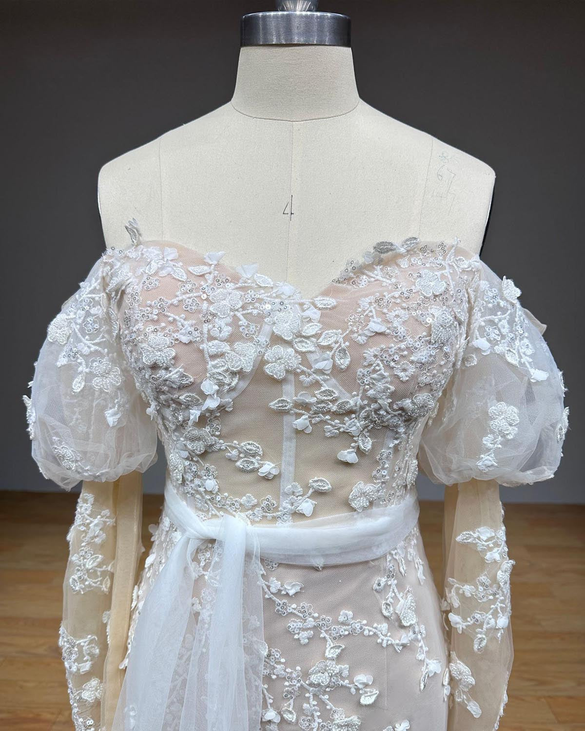 Close-up front view of the bridal bodice on a dress form, showcasing a sweetheart dip neckline, draped off-the-shoulder straps, and intricate beaded lace embroidery.