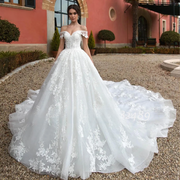 Front full view of a model wearing an off-shoulder sequin beaded ball gown wedding dress with a majestic lace-appliqued cathedral train in an outdoor setting.