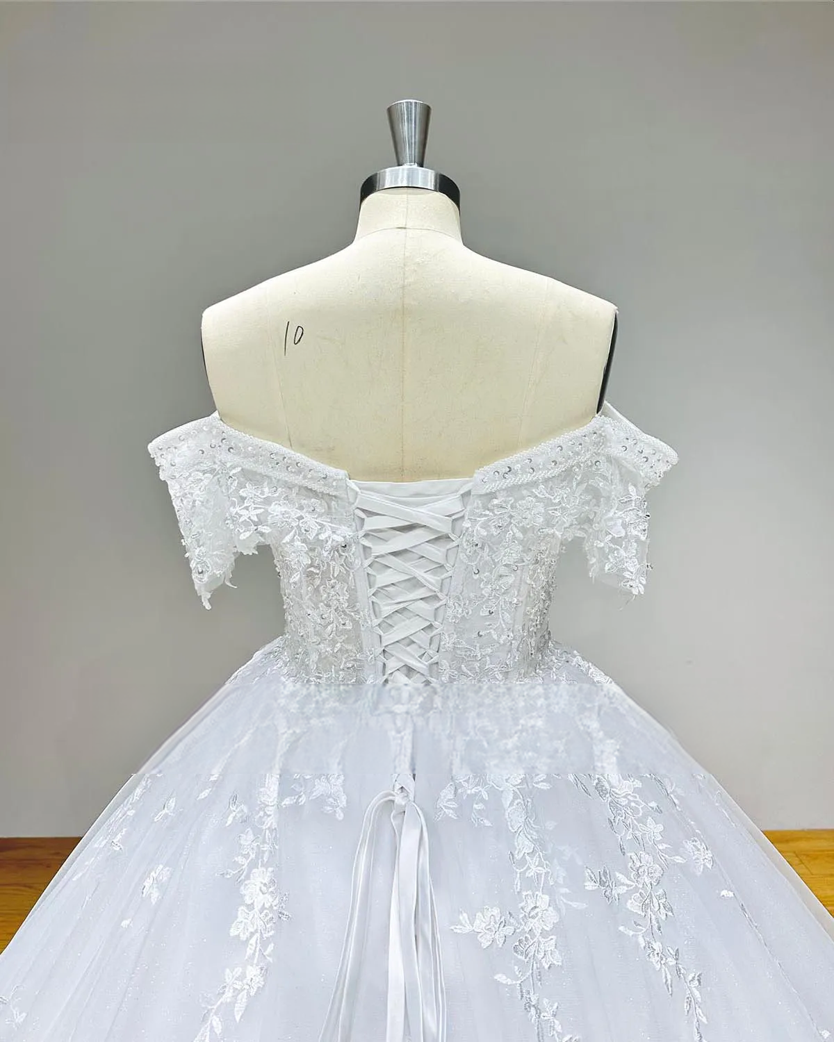 Close-up of the back of the off-shoulder sequin beaded ball gown wedding dress, detailing the adjustable lace-up corset back and intricate lace sleeves.