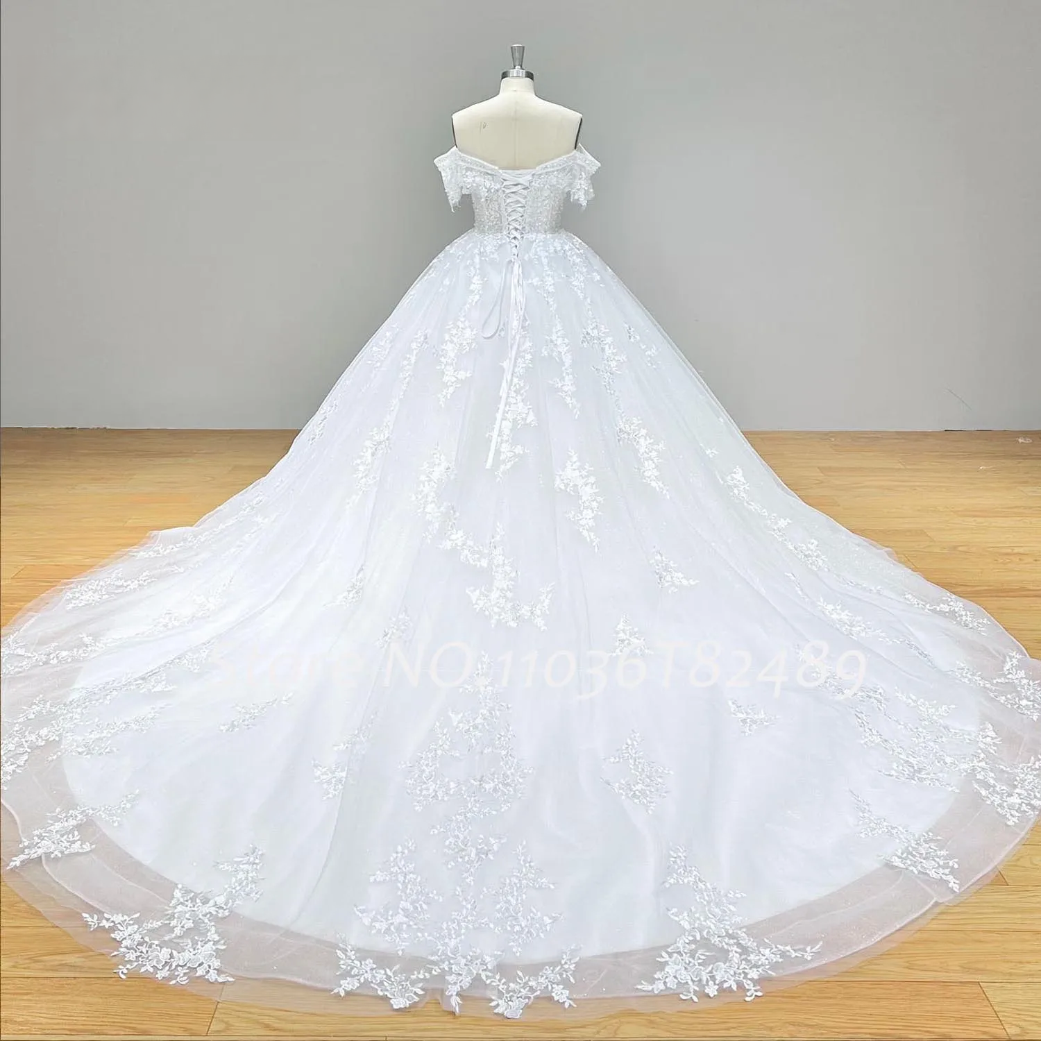 Rear view of the off-shoulder sequin beaded ball gown wedding dress on a mannequin, illustrating the expansive cathedral-length train adorned with lace trim.
