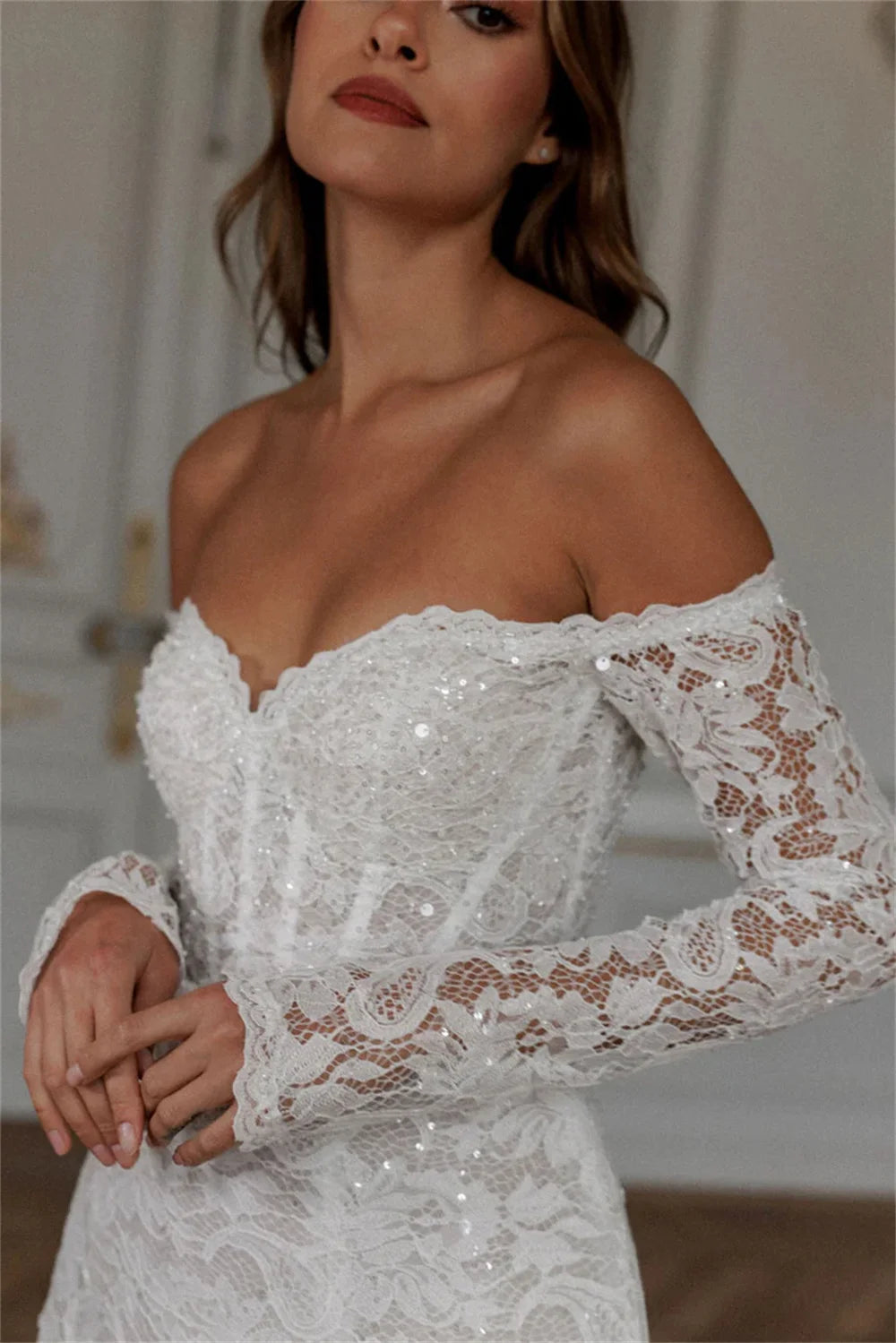 Off-the-shoulder long sleeve short wedding dress with a heavily embroidered lace pattern torso, styled elegantly for a modern reception look or civil ceremony.