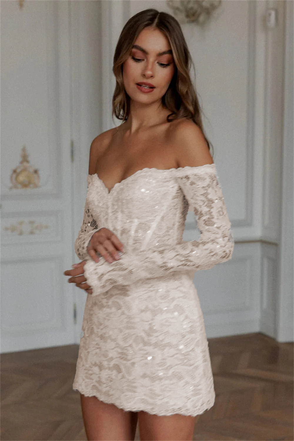 Stately soft ivory mini lace wedding dress with an off-the-shoulder straight neckline, long see-through sleeves, and a classic sheath silhouette.