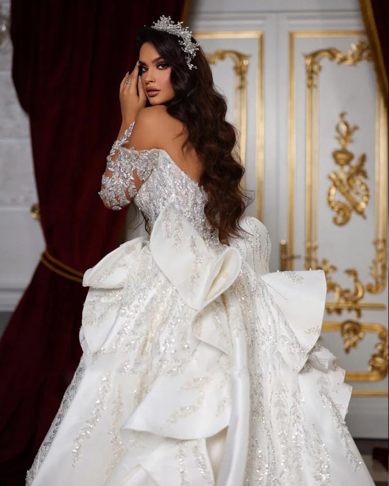 Rear view of an off-the-shoulder long-sleeve mermaid bridal gown on a mannequin, highlighting the elegant fitted silhouette, intricate beading, and sophisticated back design.