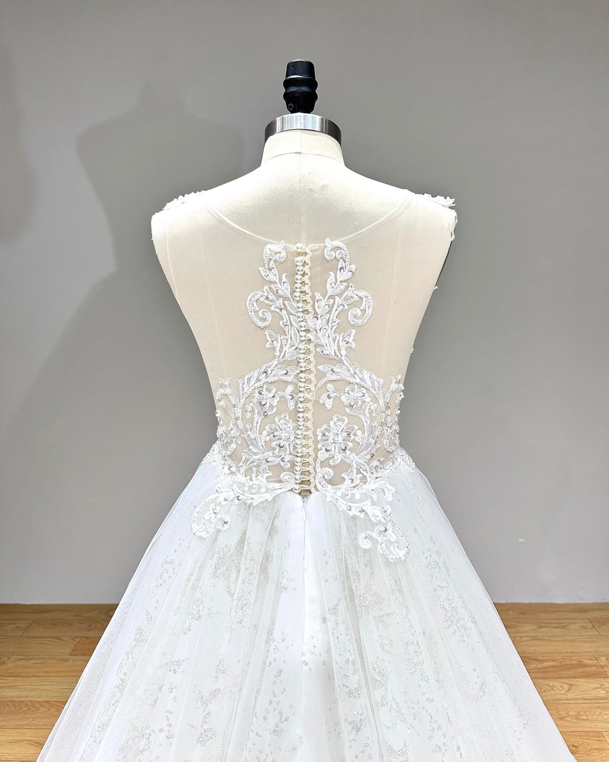 Detailed direct back view of the bridal gown focusing on the symmetrical floral lace embroidery on the sheer illusion back with a central line of pearl buttons.