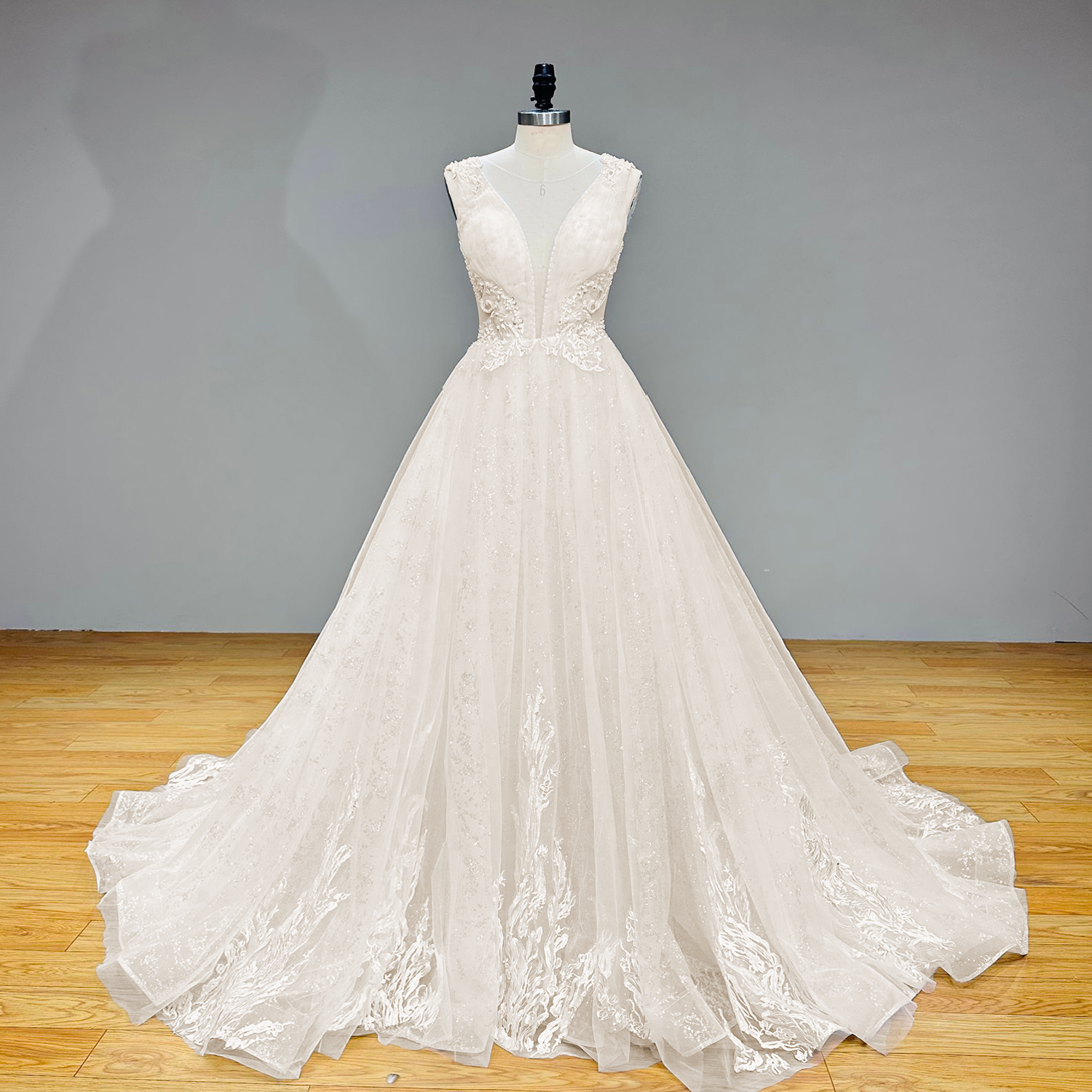 Full-length view of a curve model showcasing the sleeveless A-line wedding dress with a deep plunging V-neckline and shimmering tulle skirt inside a bridal boutique.
