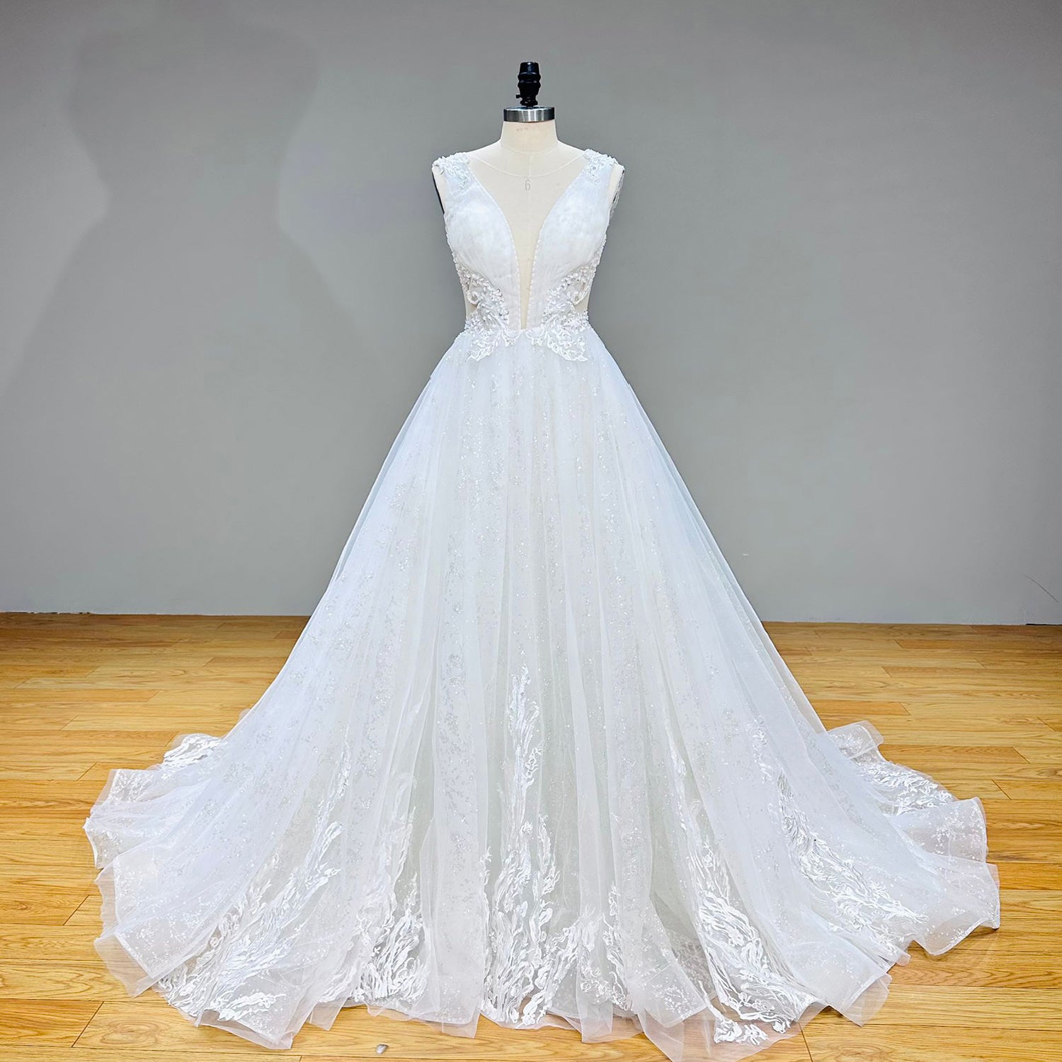 Front full-length view of the A-line bridal gown featuring an embroidered plunging bodice and layered tulle train displayed on a boutique mannequin.