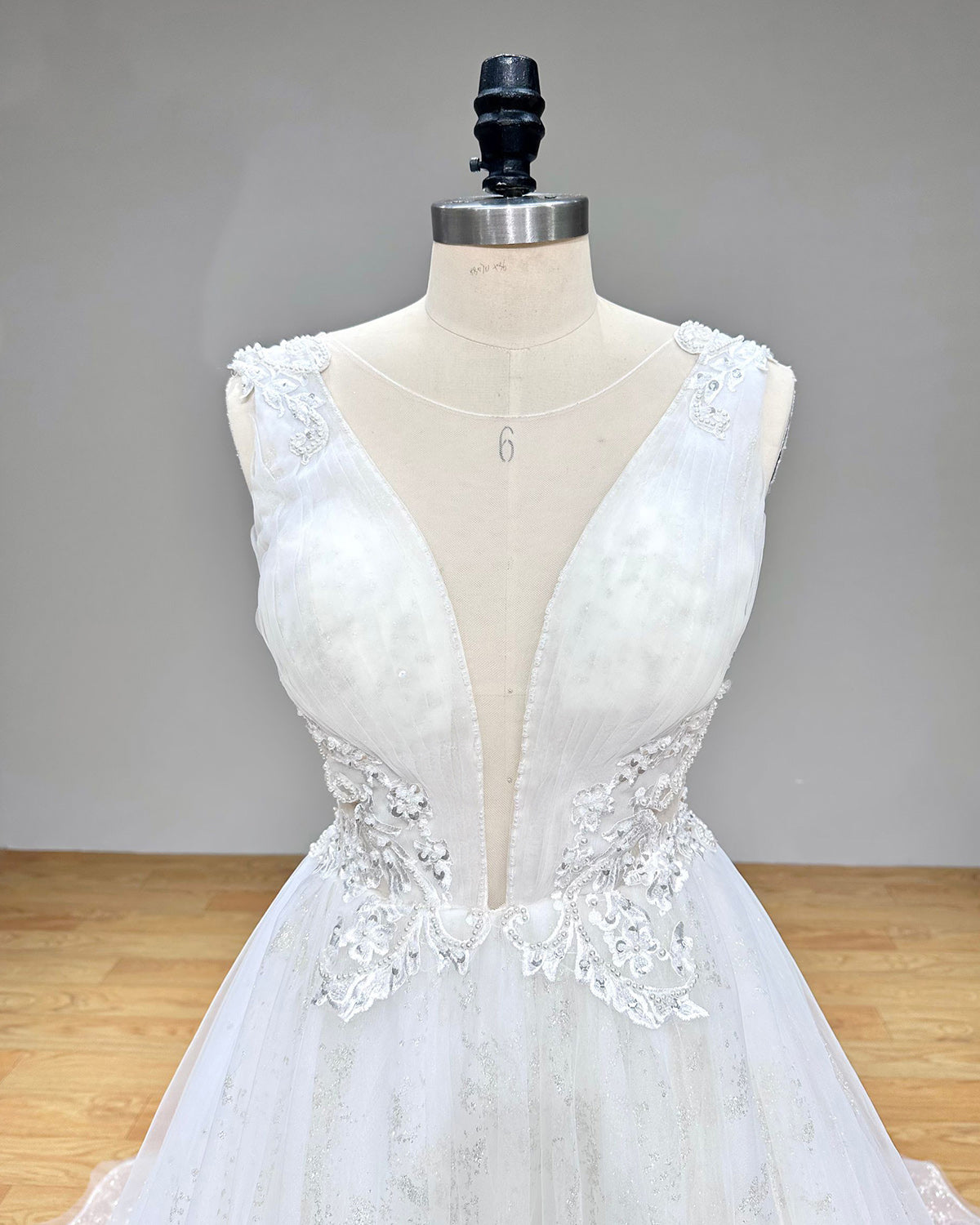 Close-up front detail of the bridal gown bodice highlighting the deep illusion V-neckline, sheer mesh panel, floral lace, and delicate pearl trim.