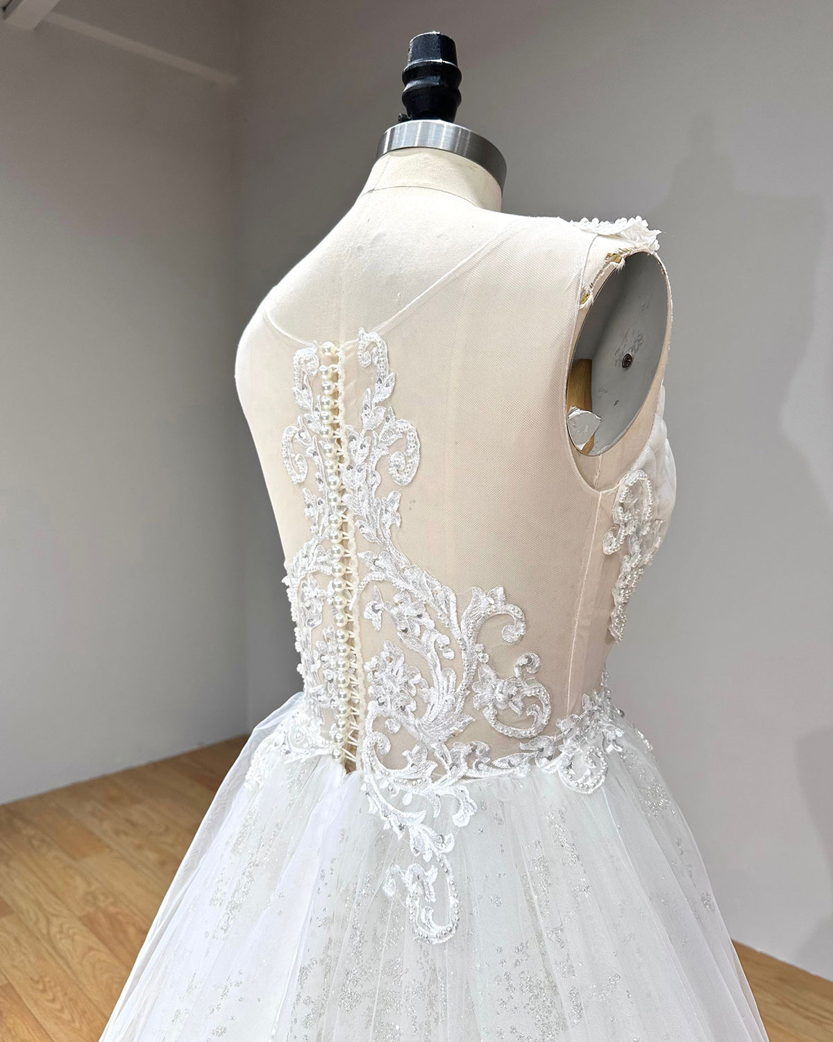 Angled close-up of the wedding dress back highlighting the sheer illusion mesh, trailing lace appliques, and classic pearl button closure along the spine.