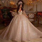 Dramatic off-the-shoulder ball gown wedding dress with a plunging V-neckline, heavily crystal-beaded corset bodice, and a voluminous shimmering glitter tulle skirt.