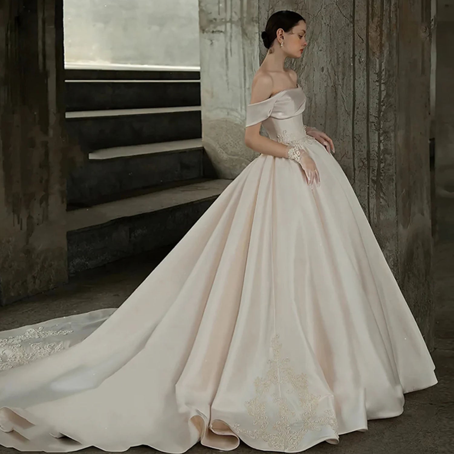 Side view of a structural off-the-shoulder satin wedding dress showcasing the draped portrait neckline and lace embroidery on the skirt hem.