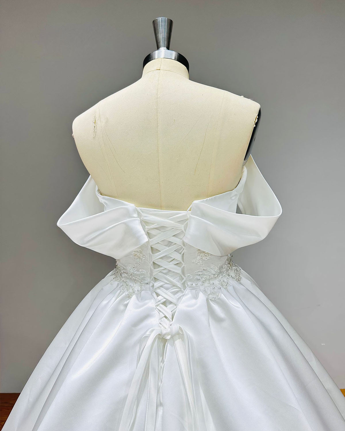 Close-up of the back of a satin bridal gown highlighting the adjustable lace-up corset closure and delicate pearl beadwork along the waist.