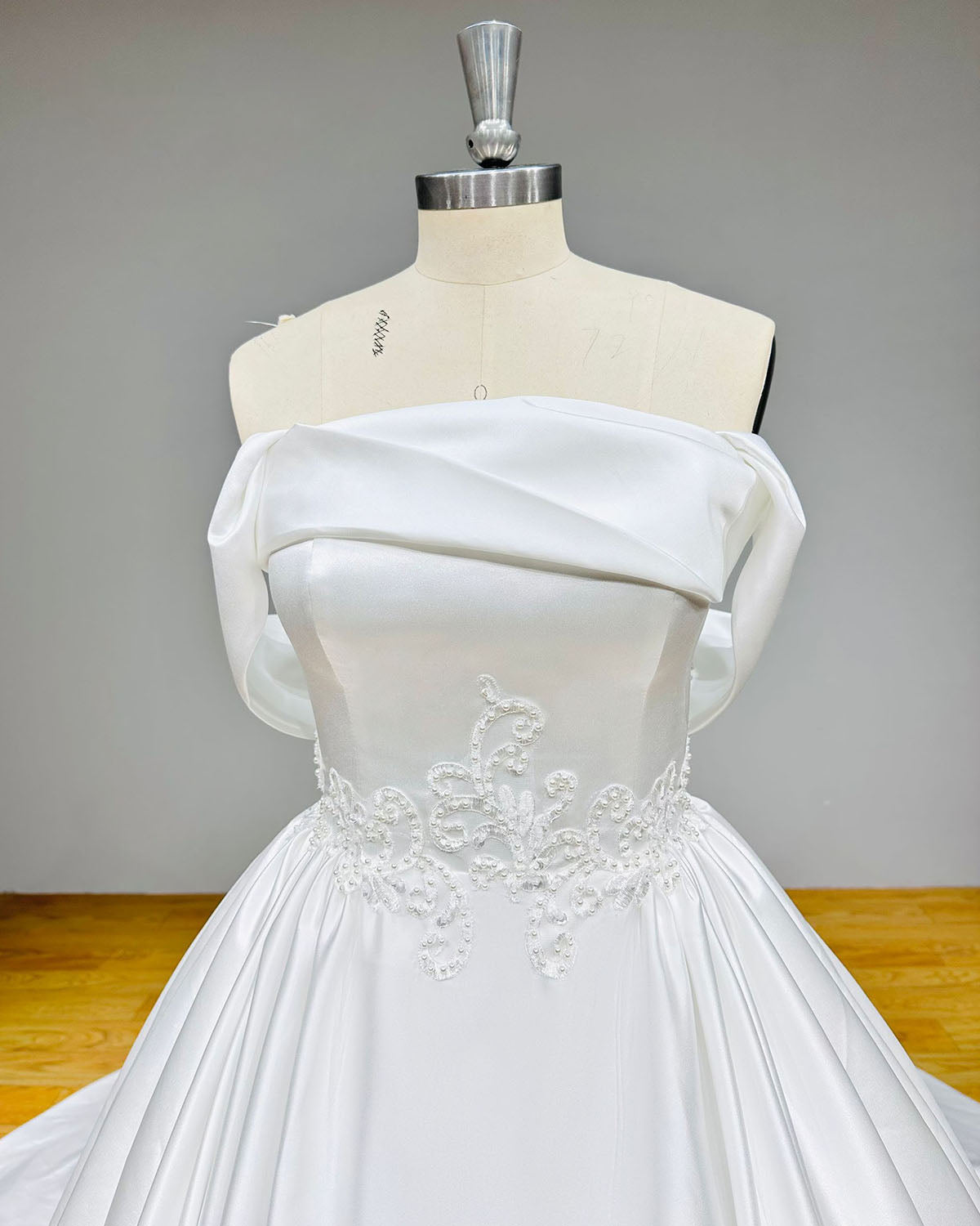 Detailed view of a structured satin wedding dress bodice featuring a folded portrait neckline and a symmetrical pearl and lace applique waistband.