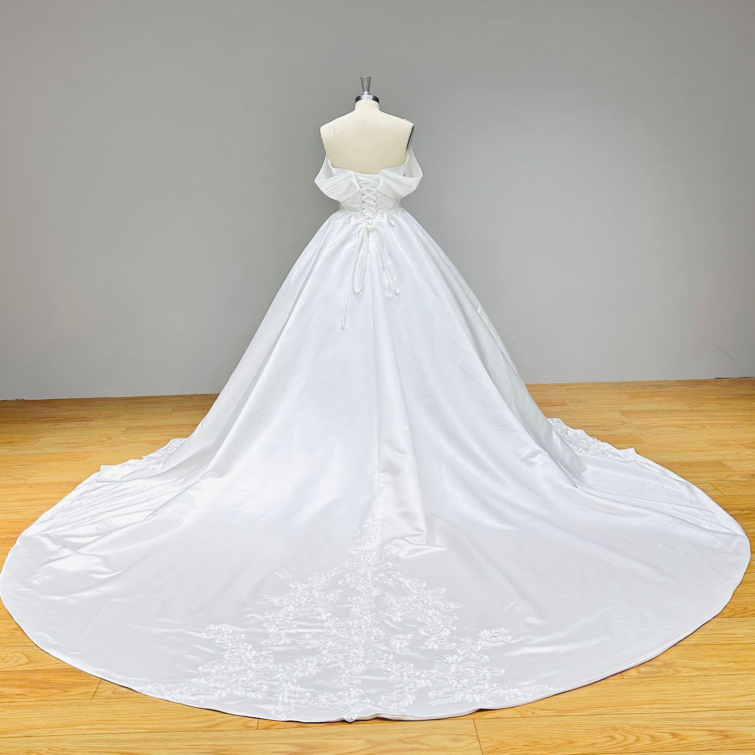 Full back view of an off-the-shoulder satin wedding gown showcasing a dramatic circular train finished with intricate lace borders.