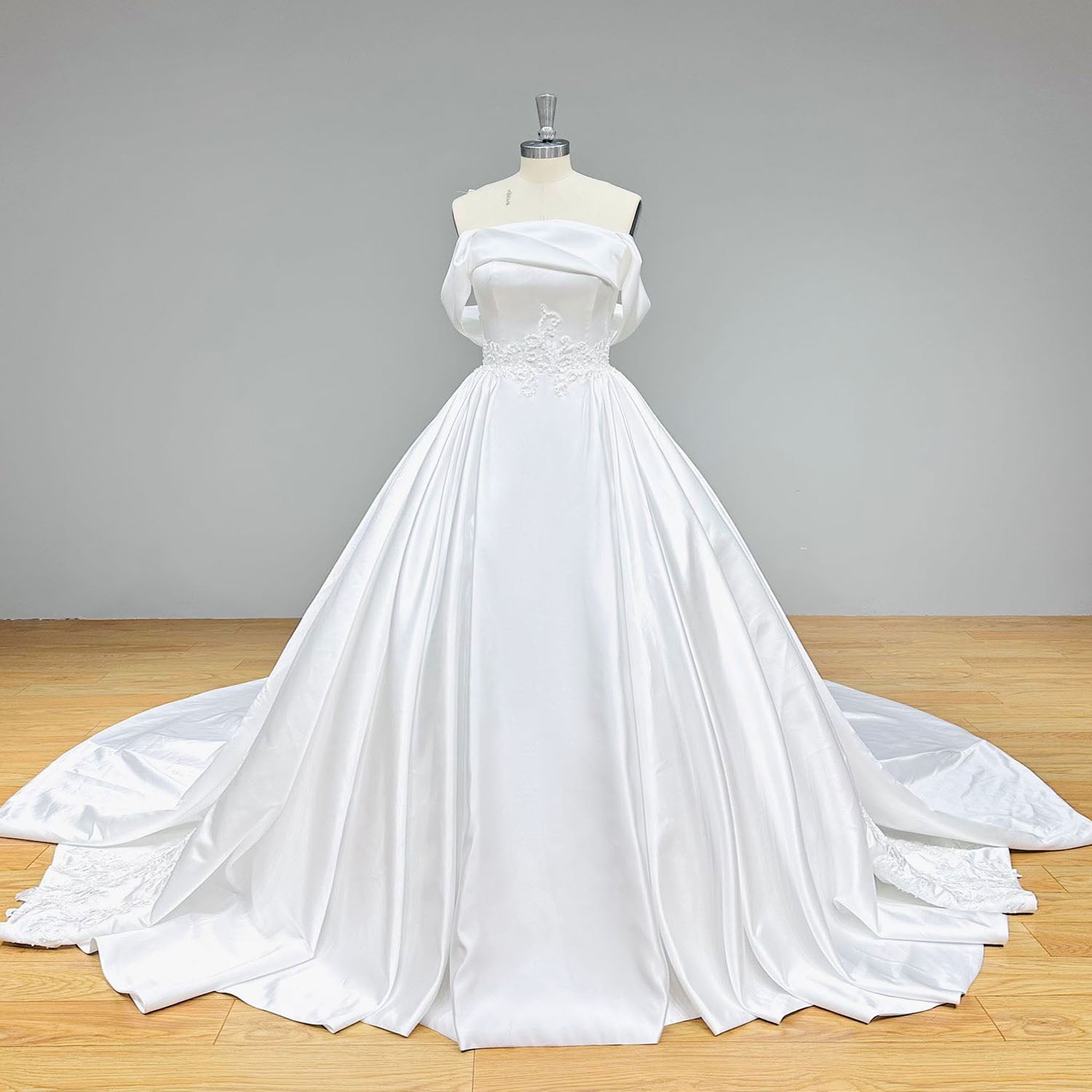 Front view of a premium quality off-the-shoulder satin ball gown bridal dress with a pleated waistline on a dress form.