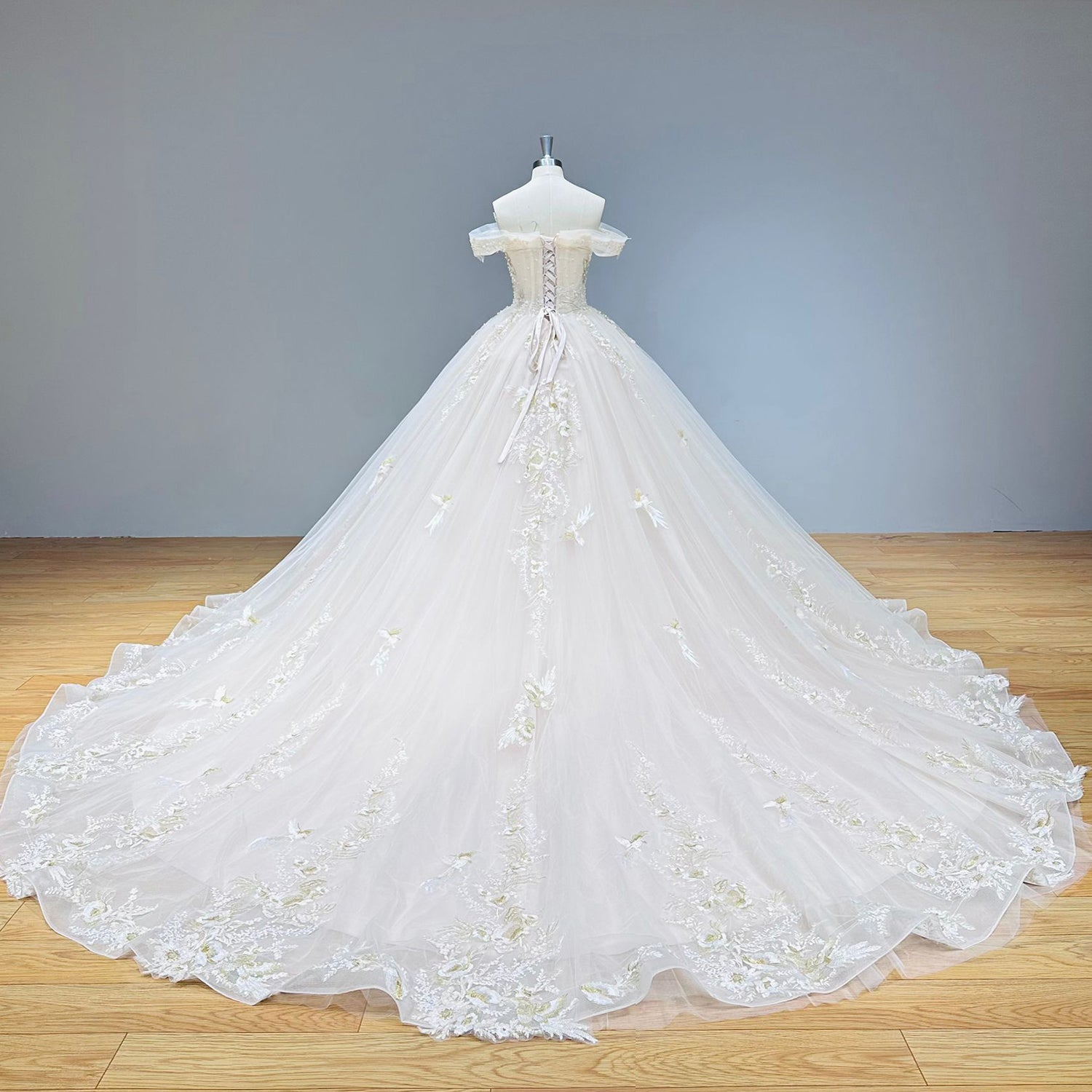 Wide back view of a champagne princess wedding dress on a mannequin, highlighting the intricate lace-up corset back and long cathedral tulle train.