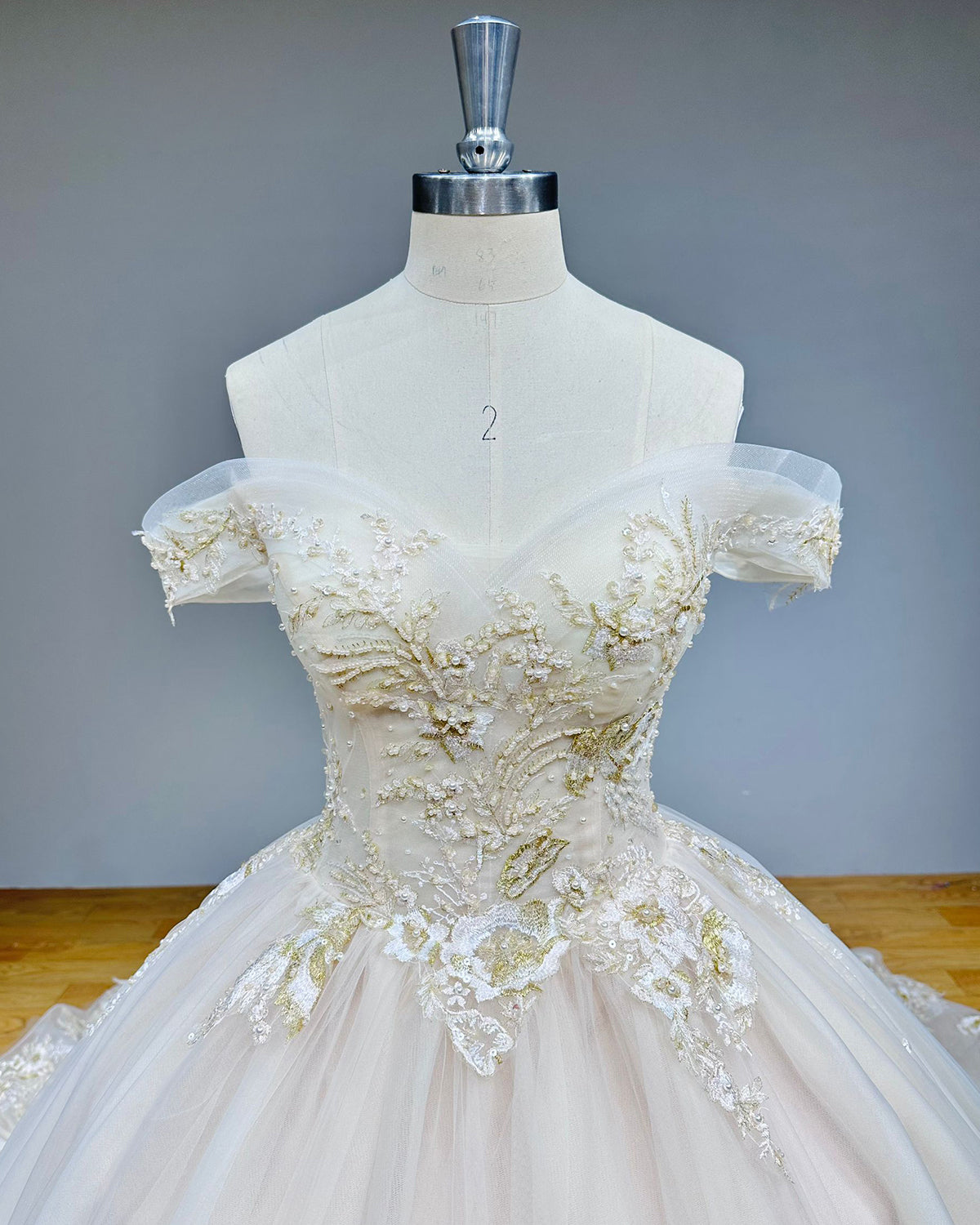 Close-up front shot of the wedding dress bodice showcasing the sweetheart neckline, sheer off-the-shoulder straps, and heavy gold sequin and bead embellishments.