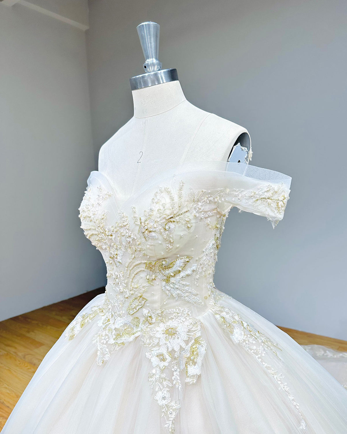 Side angle close-up of a beaded bridal gown bodice on a dress form, emphasizing the 3D lace appliques and delicate tulle draping.