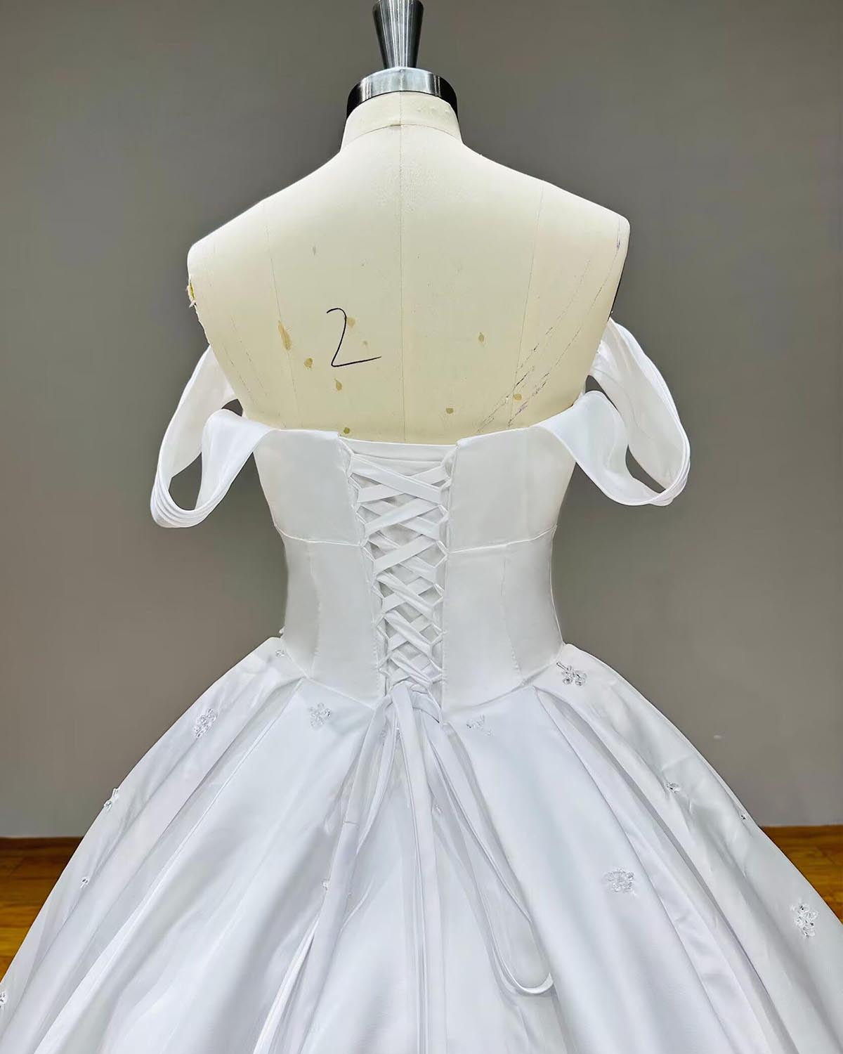 Close-up back view of a satin bridal gown highlighting an adjustable lace-up corset back closure and elegant cuffed off-the-shoulder straps.