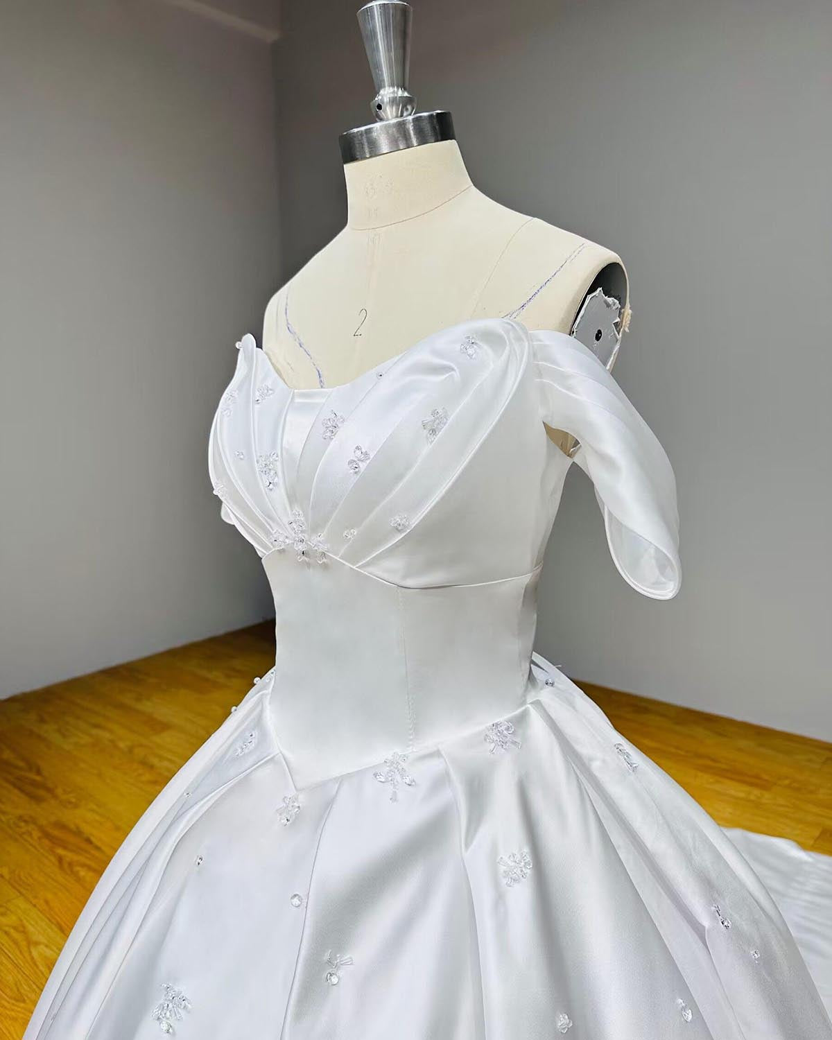 Three-quarter close-up of a white satin wedding gown bodice detailing romantic crossover pleating on the bust and tiny floral crystal motifs.