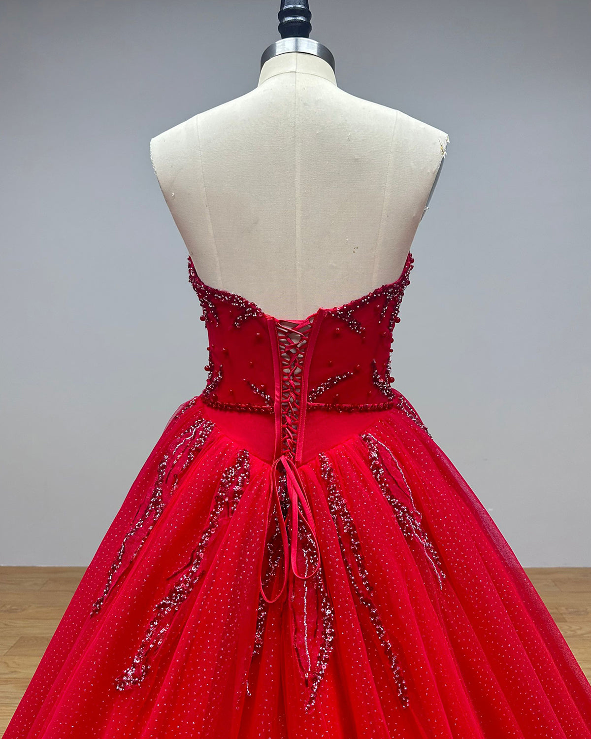 Close-up back detail of a red bridal gown corset showing a secure lace-up satin closure surrounded by intricate tonal beadwork, pearls, and shimmering embroidery lines.