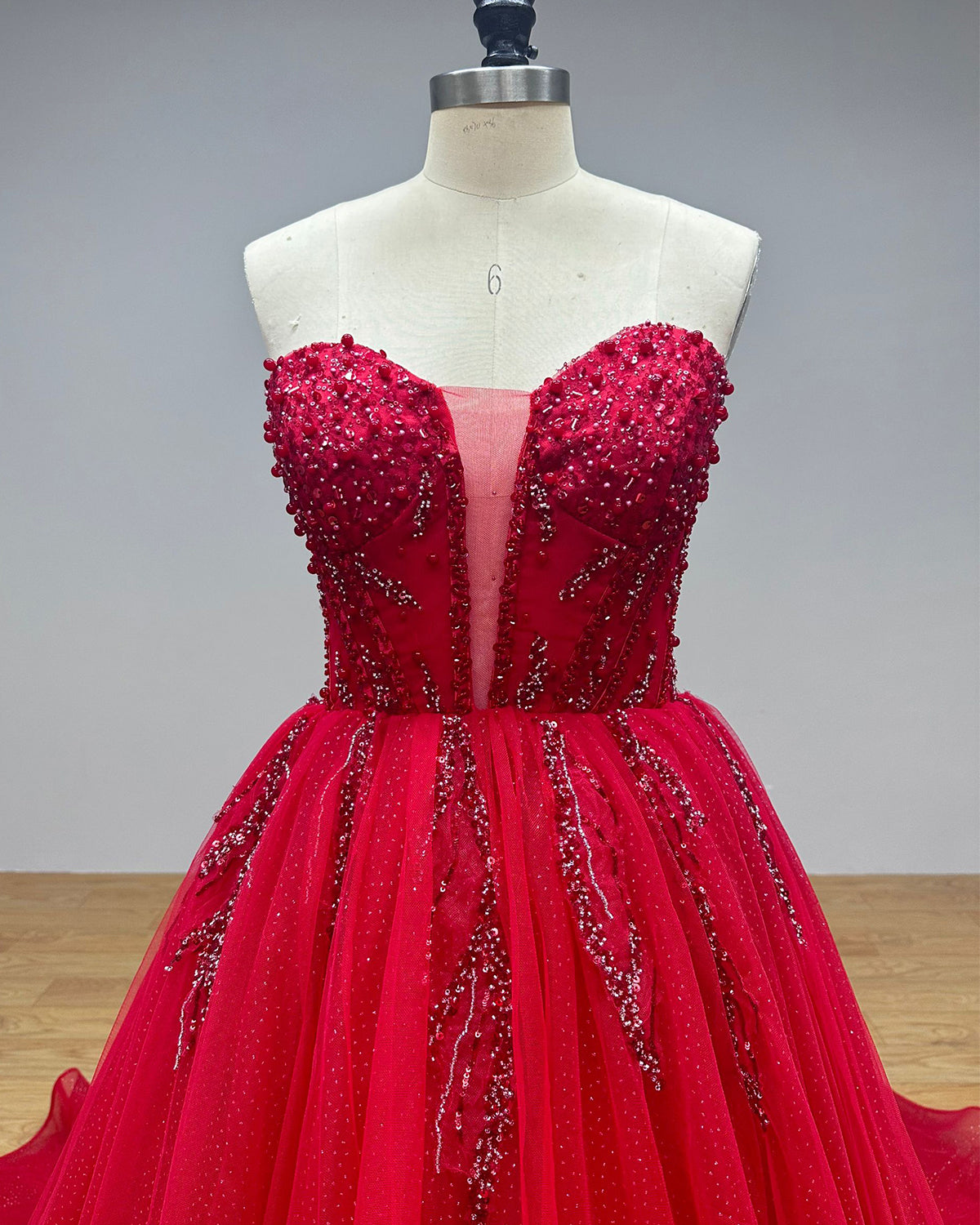 Close-up bodice view of a red strapless wedding gown featuring dense sequin beading on the cups, structured supportive seams, and a sheer mesh plunge insert.