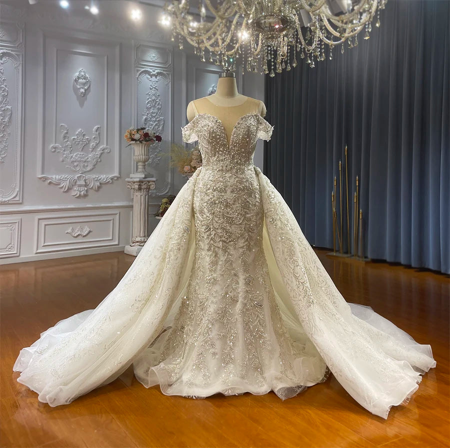Elegant ivory mermaid bridal gown with a detachable skirt attached, showcasing the shimmering hand-beaded lace bodice and wide cathedral train in a professional bridal showroom.