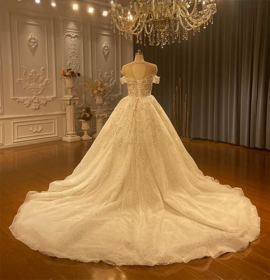Rear perspective of a 2-in-1 wedding dress with the overskirt, highlighting the elegant lace-up corset back, illusion mesh detailing, and a grand, sparkling cathedral-length train.