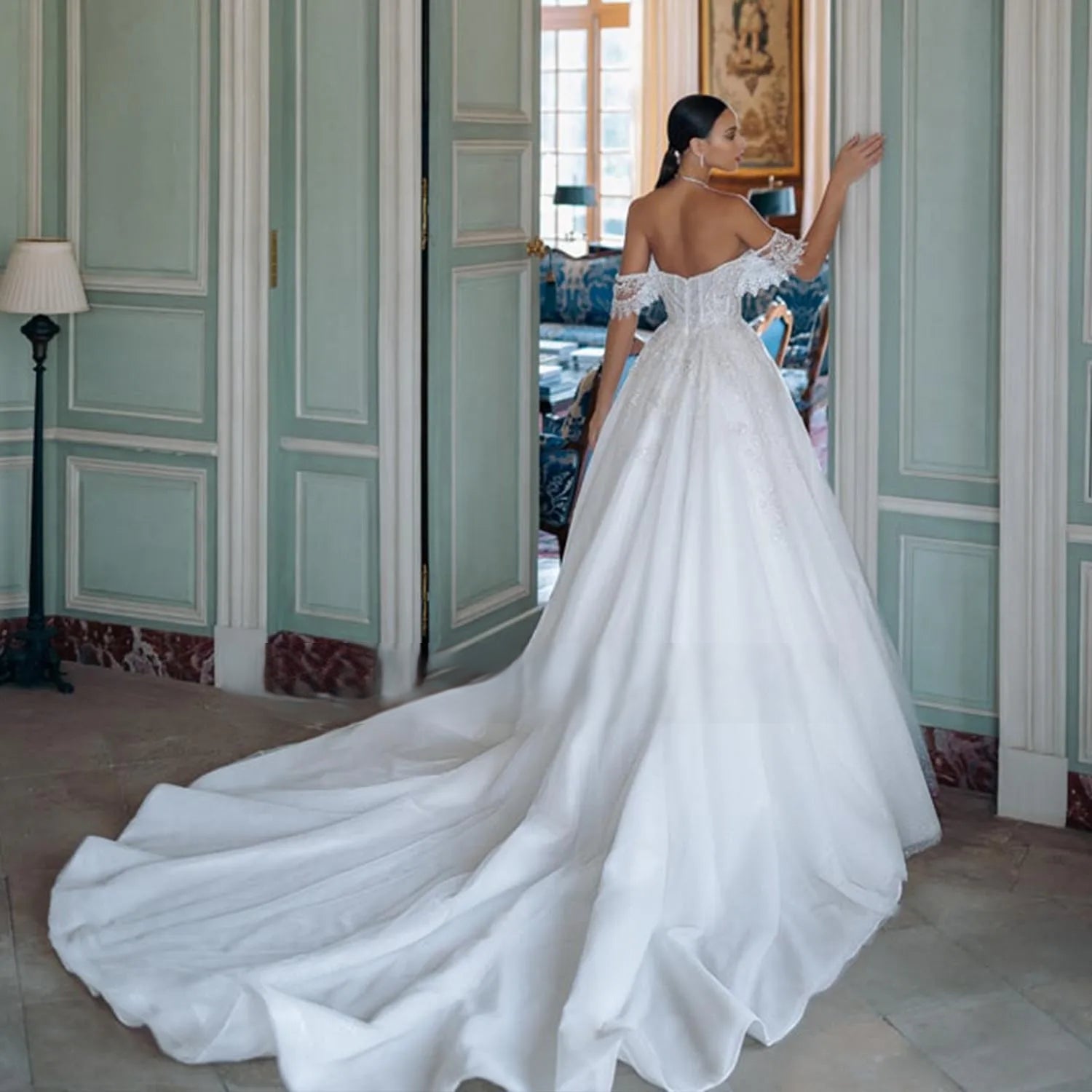 Back view of a glamorous backless bridal gown featuring a long, cascading tulle cathedral train and delicate lace detailing along the portrait neckline.