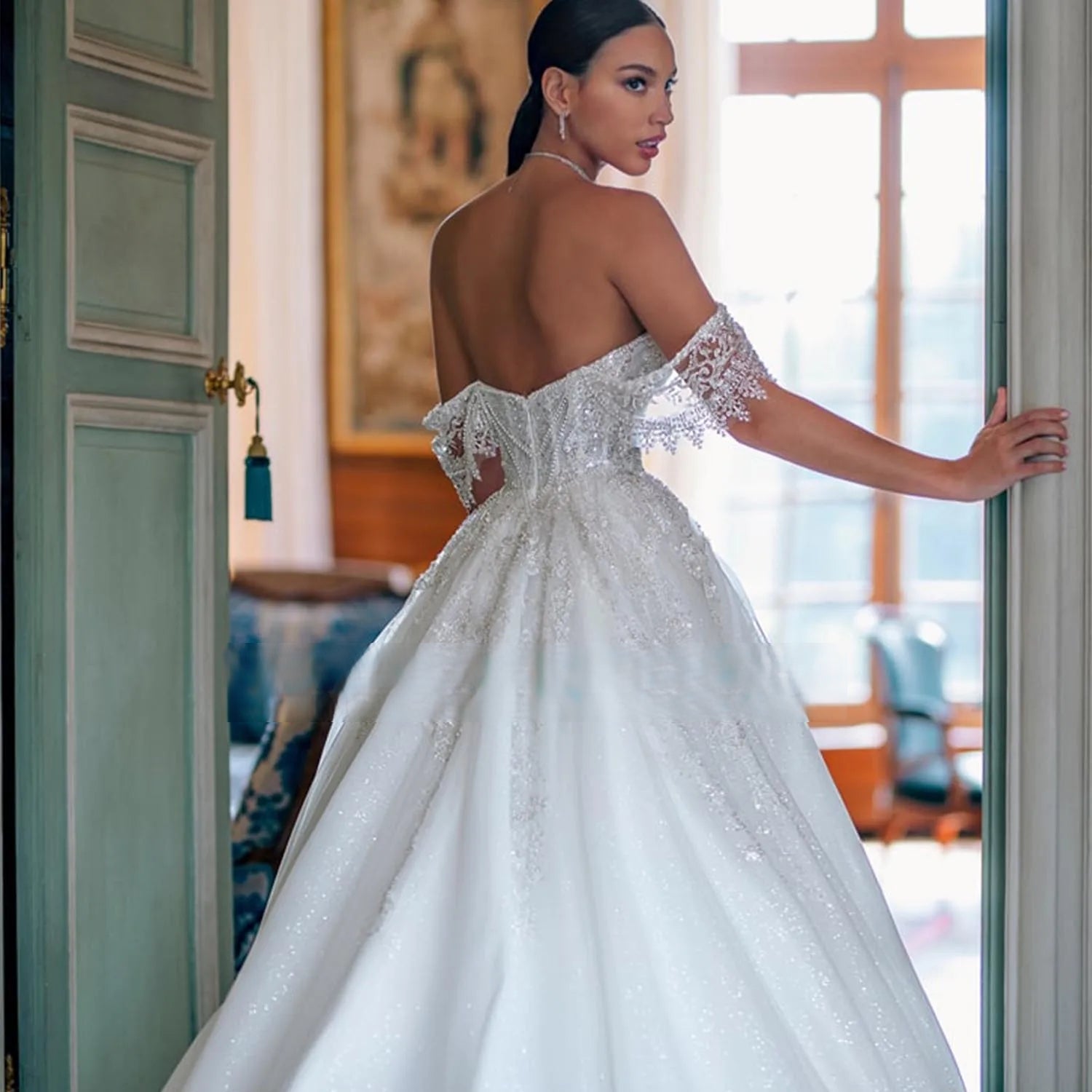 Close-up rear angle of a luxury wedding dress showing a low open back, structured corset boning, and sheer embroidered lace off-the-shoulder straps.