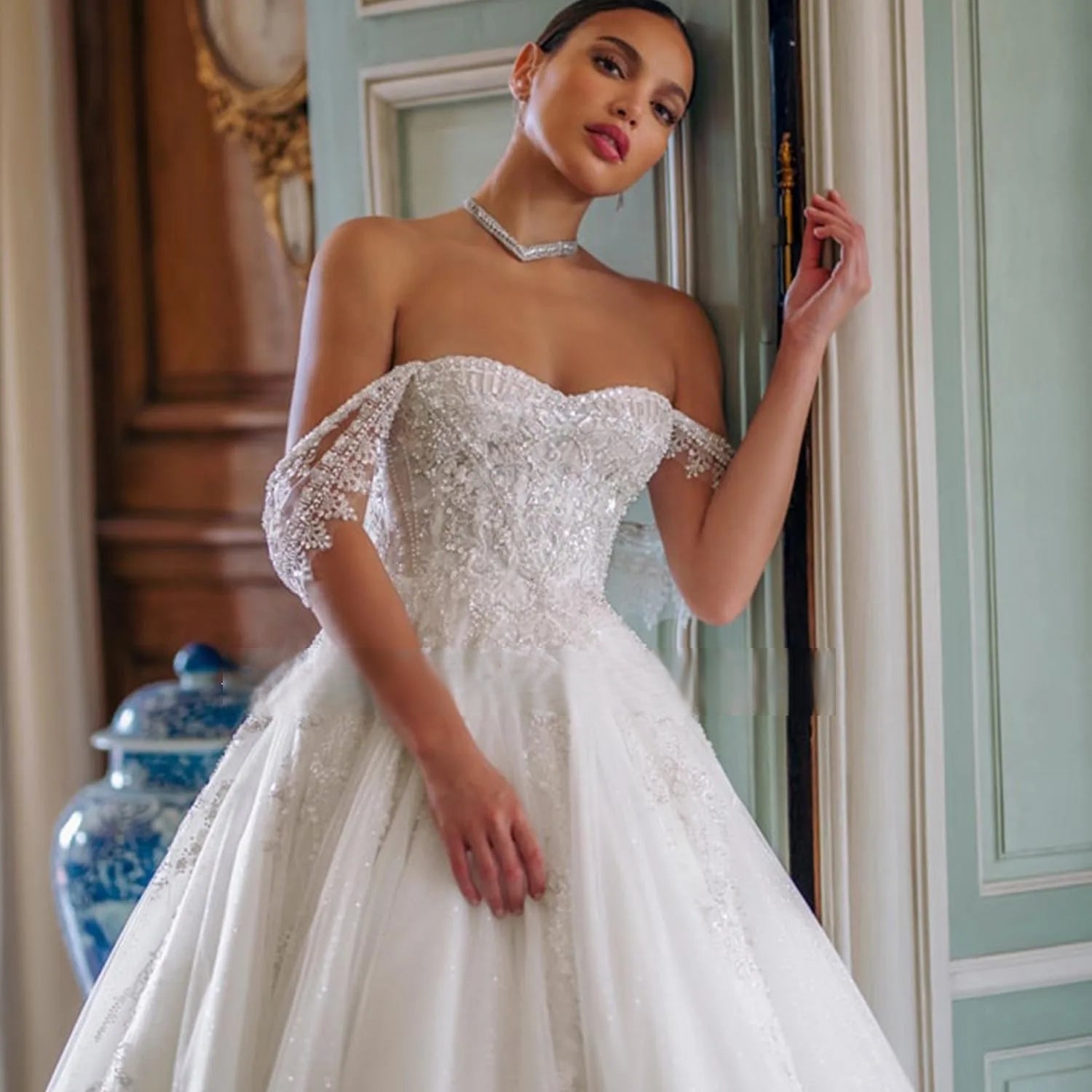 High-fashion bride posing in a beaded off-the-shoulder tulle wedding dress, accessorized with a modern diamond chevron choker necklace.